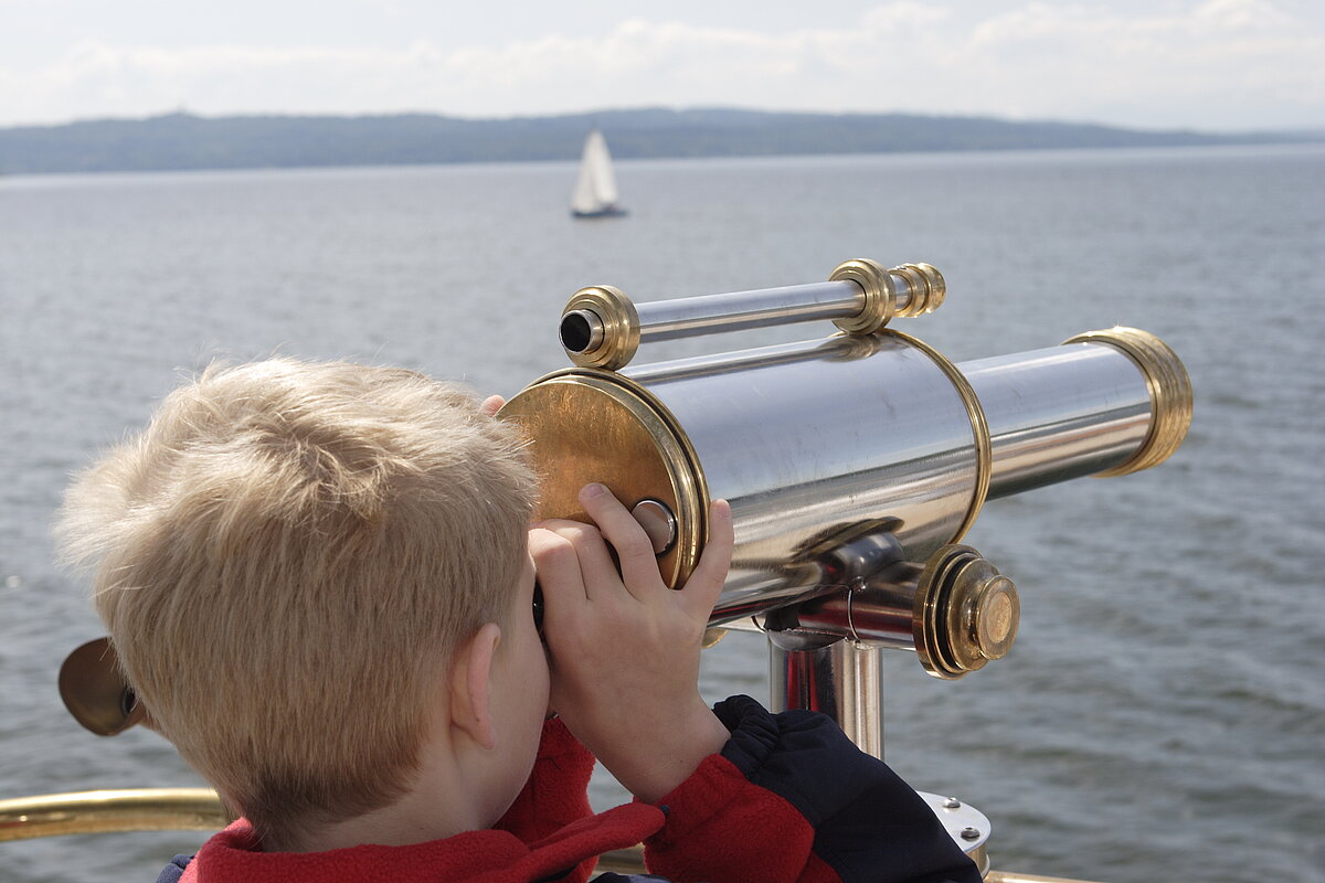 Kind blickt durch ein Fernrohr auf dem Raddampfer